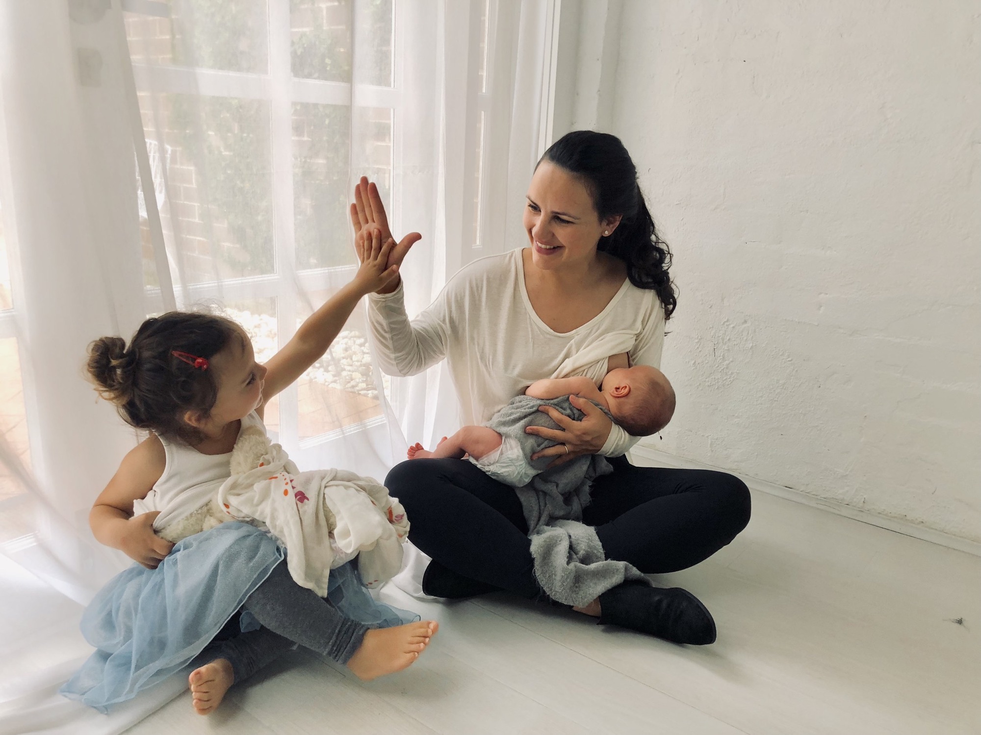 Tammy sitting on the floor with her baby on her lap, high-fiving her young daughter